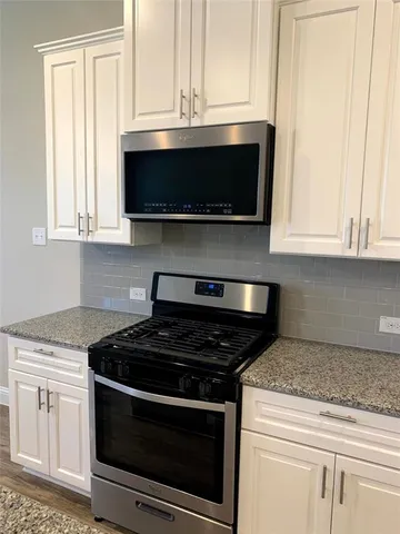 a kitchen with stainless steel appliances granite countertop white cabinets and a stove top oven