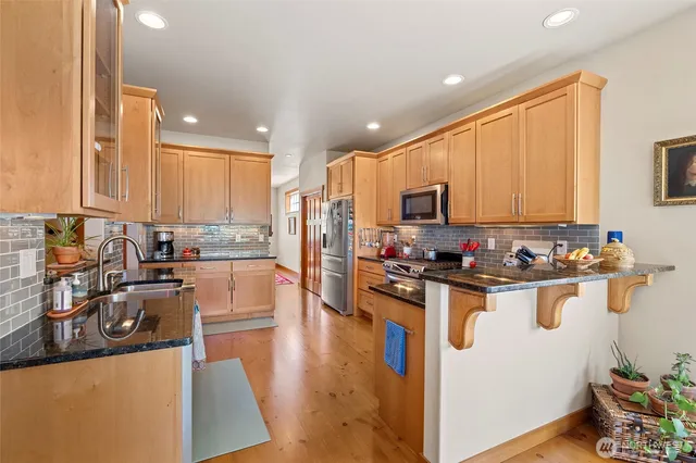 a kitchen with stainless steel appliances granite countertop a stove top oven a sink dishwasher and a microwave with wooden floor