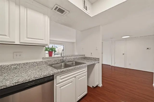 a kitchen with granite countertop a sink and dishwasher cabinets with wooden floor