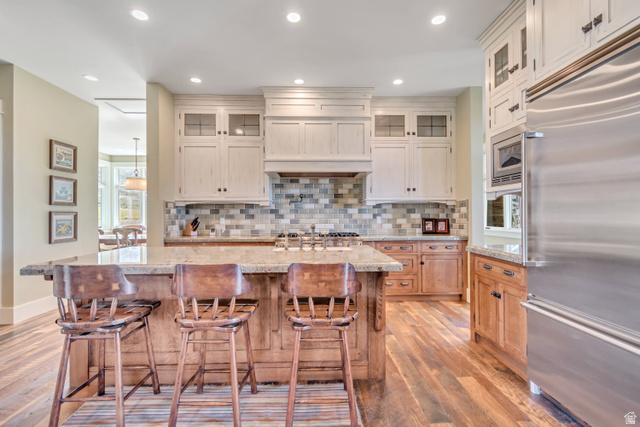 2579 Splendor Valley Road Kamas, UT 84036 - Photo 86 of 87 Kitchen with glass fronted cabinets, built in appliances, a center island with sink, light wood-style floors, and a kitchen bar