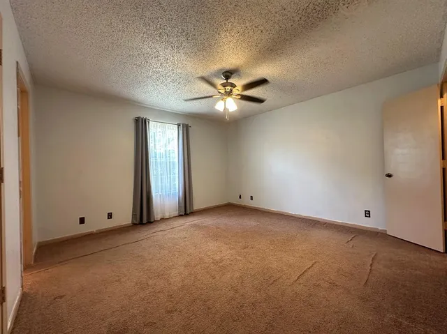 an empty room with chandelier fan and windows
