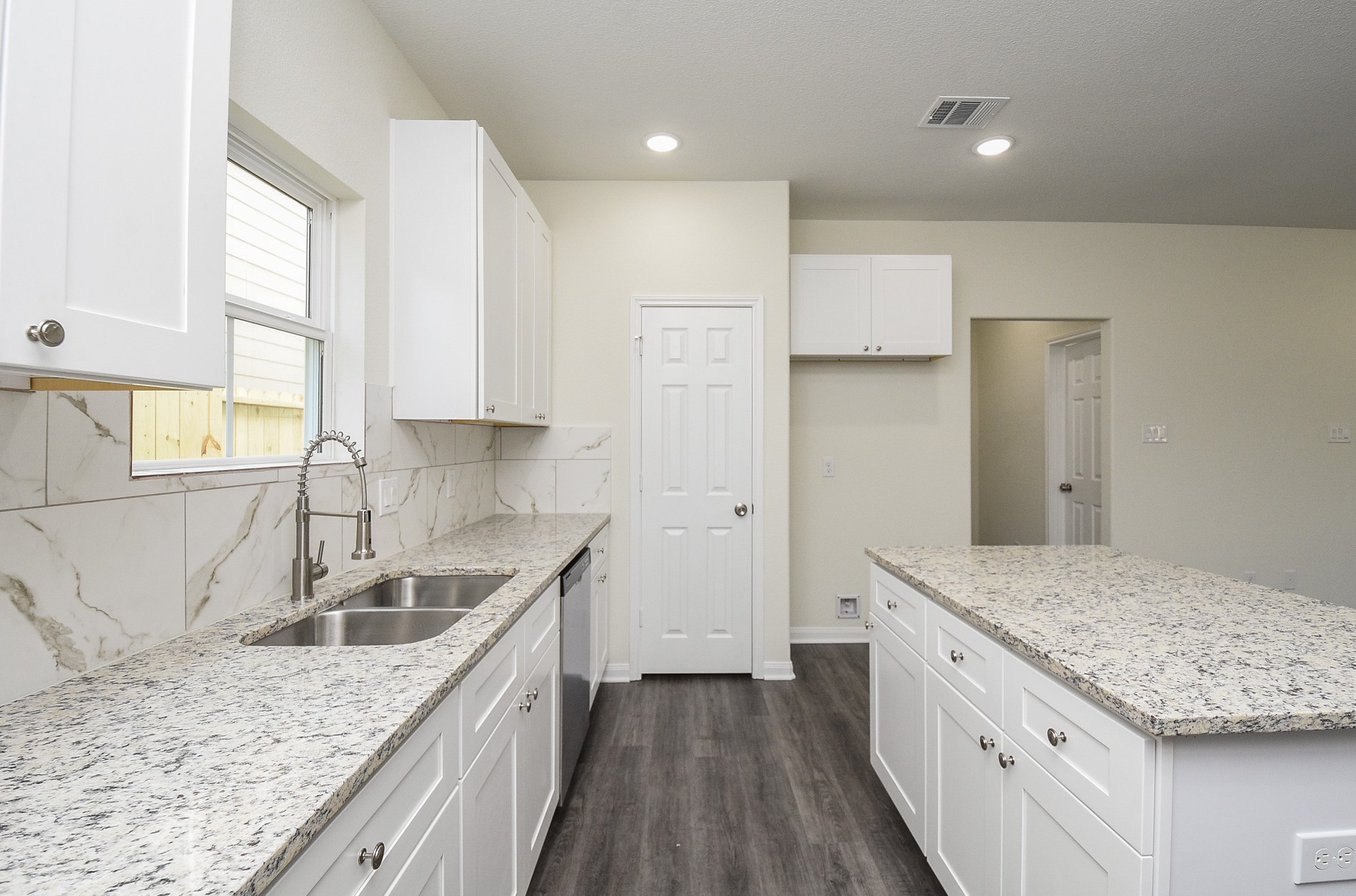 2811 Topiary Lane Houston, TX 77014 - Photo 14 of 32 Modern kitchen interior with white cabinets, granite countertops, and stainless steel sink under a window, with neutral wall colors and wood flooring.