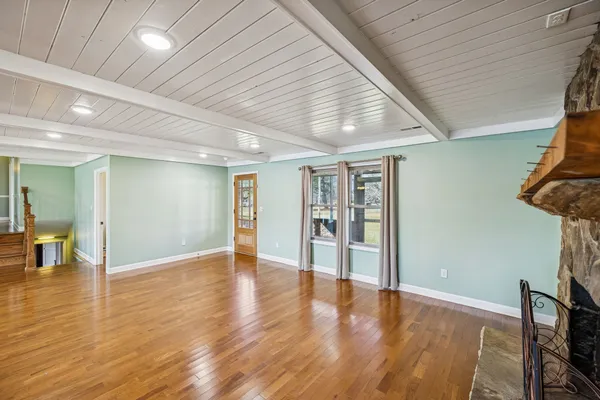 a view of an empty room with wooden floor fireplace and a window
