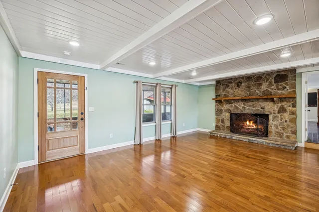 a view of an empty room with wooden floor fireplace and a window