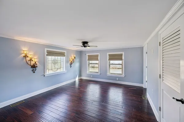 an empty room with wooden floor chandelier fan and windows