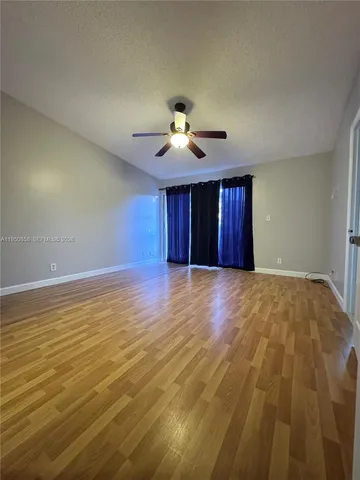 a view of an empty room with wooden floor ceiling fan and windows