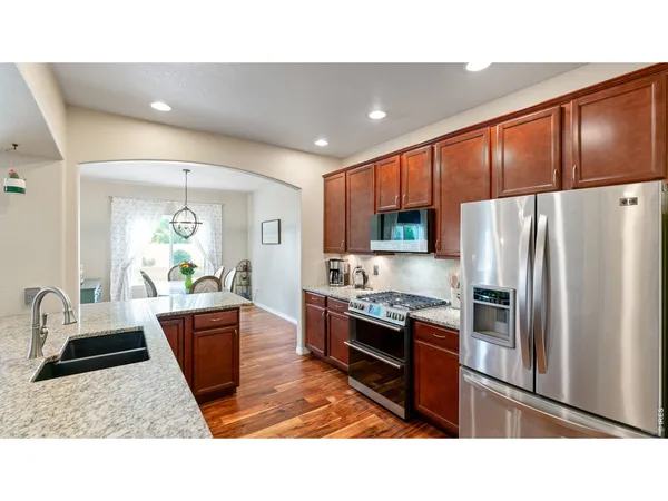 a kitchen with stainless steel appliances granite countertop a refrigerator a sink dishwasher a stove with wooden cabinets and floor