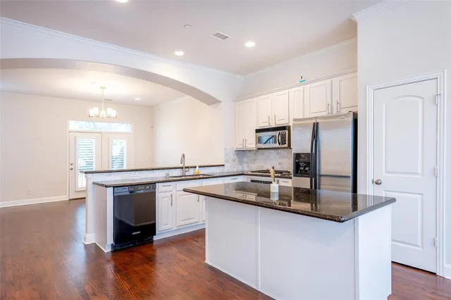 a kitchen with stainless steel appliances granite countertop a sink a stove a refrigerator and white cabinets with wooden floor