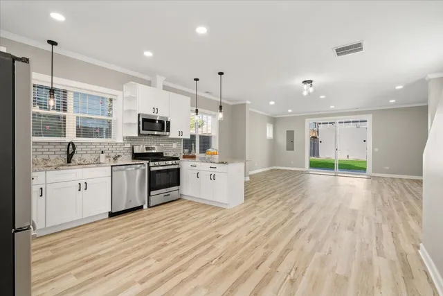 a kitchen with stainless steel appliances kitchen island granite countertop a stove a sink and white cabinets with wooden floor