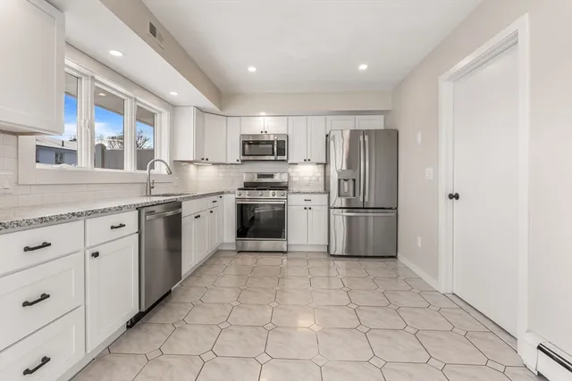 a kitchen with stainless steel appliances granite countertop a sink a stove a refrigerator and white cabinets