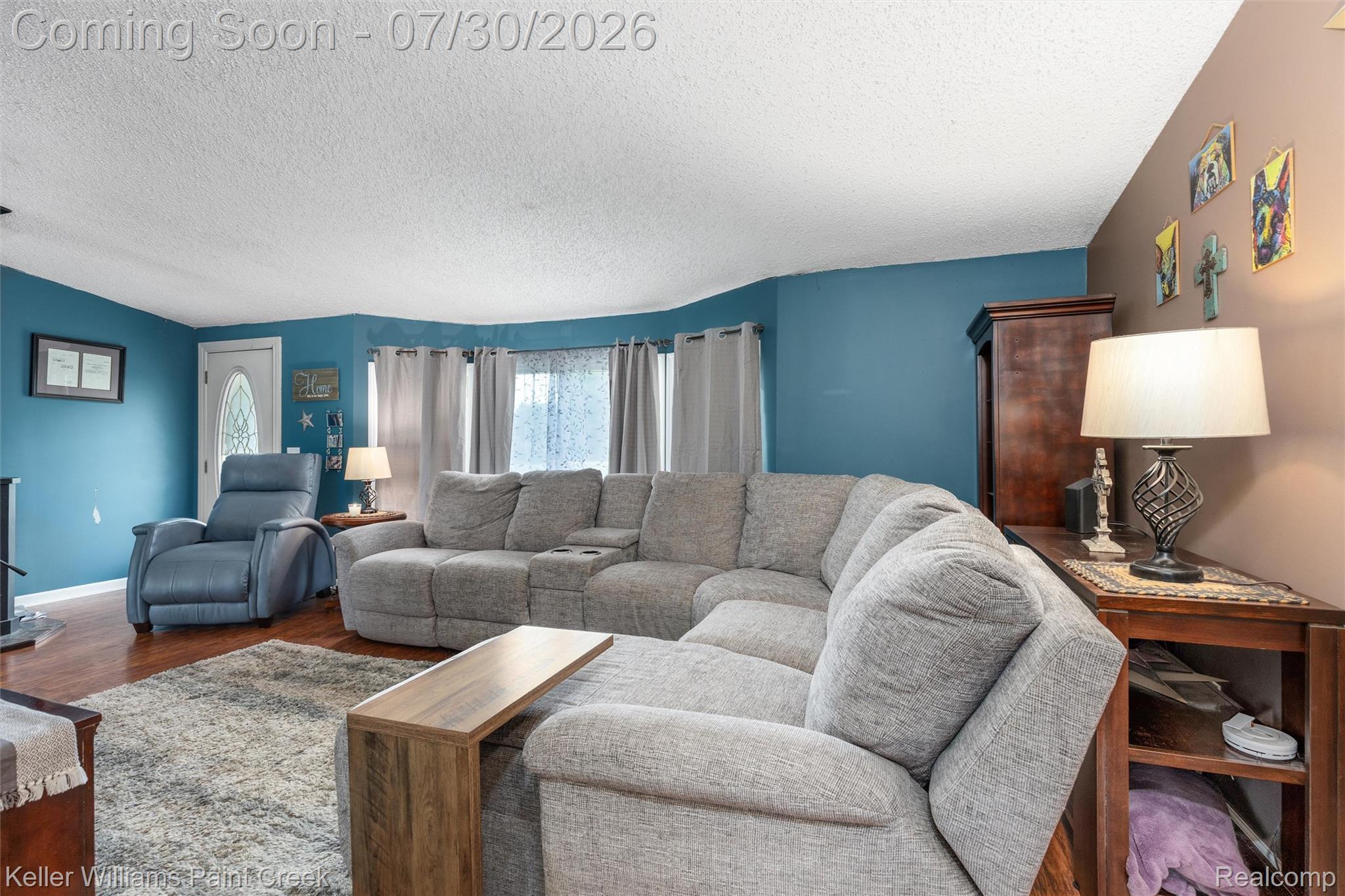 7544 Ravenswood Road Goodells, MI 48027 - Photo 15 of 42 Living area featuring wood-finish flooring, a decorative front door with an oval glass insert, and a wall of windows with drapery