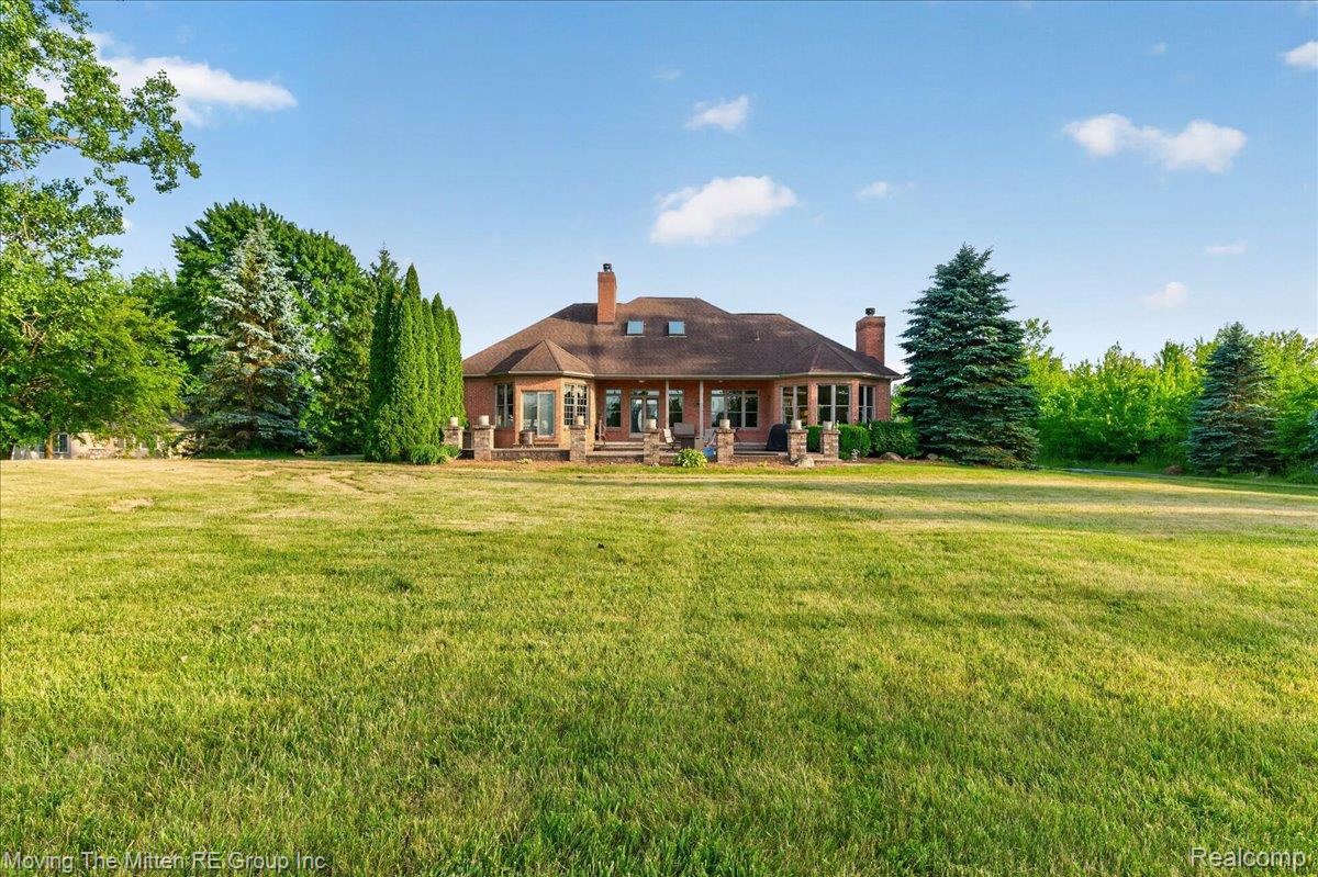 39750 Willow Road New Boston, MI 48164 - Photo 47 of 68 Expansive green lawn with a red brick exterior residence featuring multiple chimneys, a dark shingle roof, and numerous glass doors and windows
