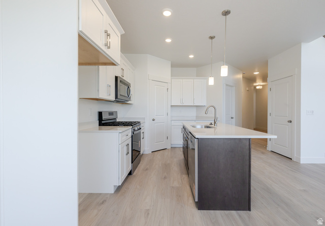 4720 Heartwood Road, Unit 438 Mapleton, UT 84664 - Photo 8 of 19 Kitchen with stainless steel appliances, dual tone cabinets, light wood-style floors, a kitchen island with sink, and decorative light fixtures