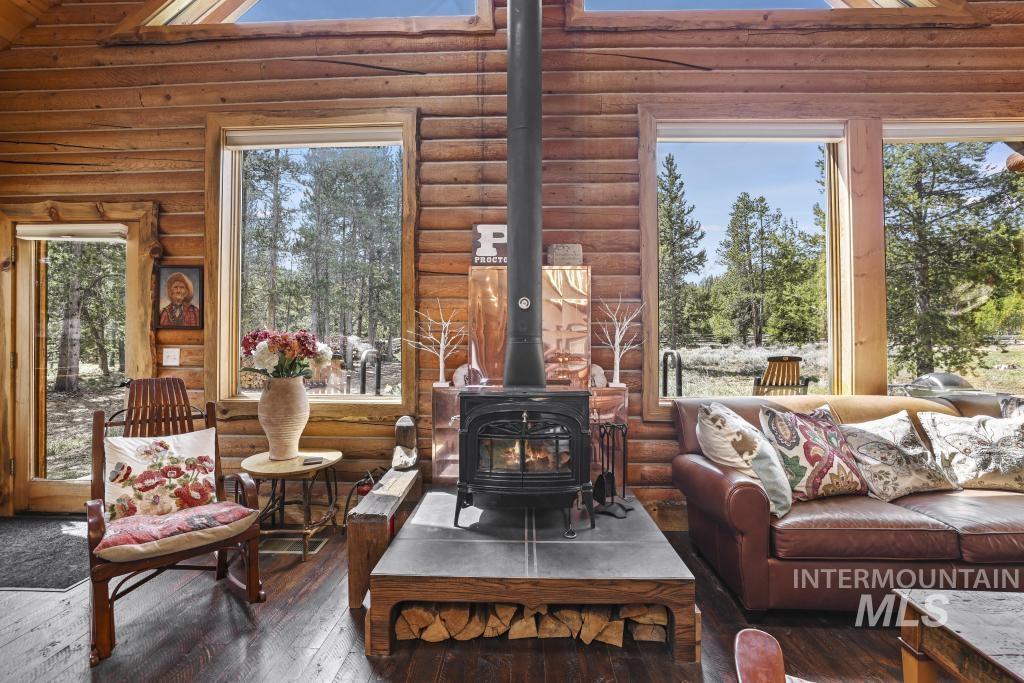65 Goat Creek Way Stanley, ID 83278 - Photo 12 of 32 Wood-clad interior featuring a cast iron wood-burning stove with a stone hearth, hardwood flooring, and multiple large windows
