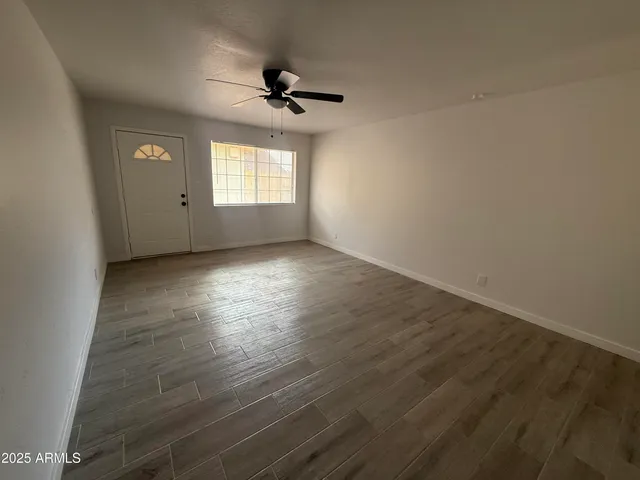 an empty room with wooden floor fan and windows