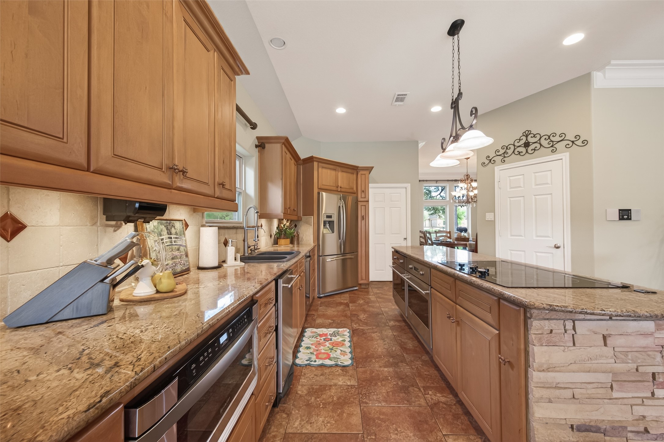 17603 Bending Cypress Road Cypress, TX 77429 - Photo 14 of 43 The kitchen includes a large island with a cooktop and ample storage, enhanced by warm lighting and stylish tile flooring. Perfect for culinary enthusiasts.