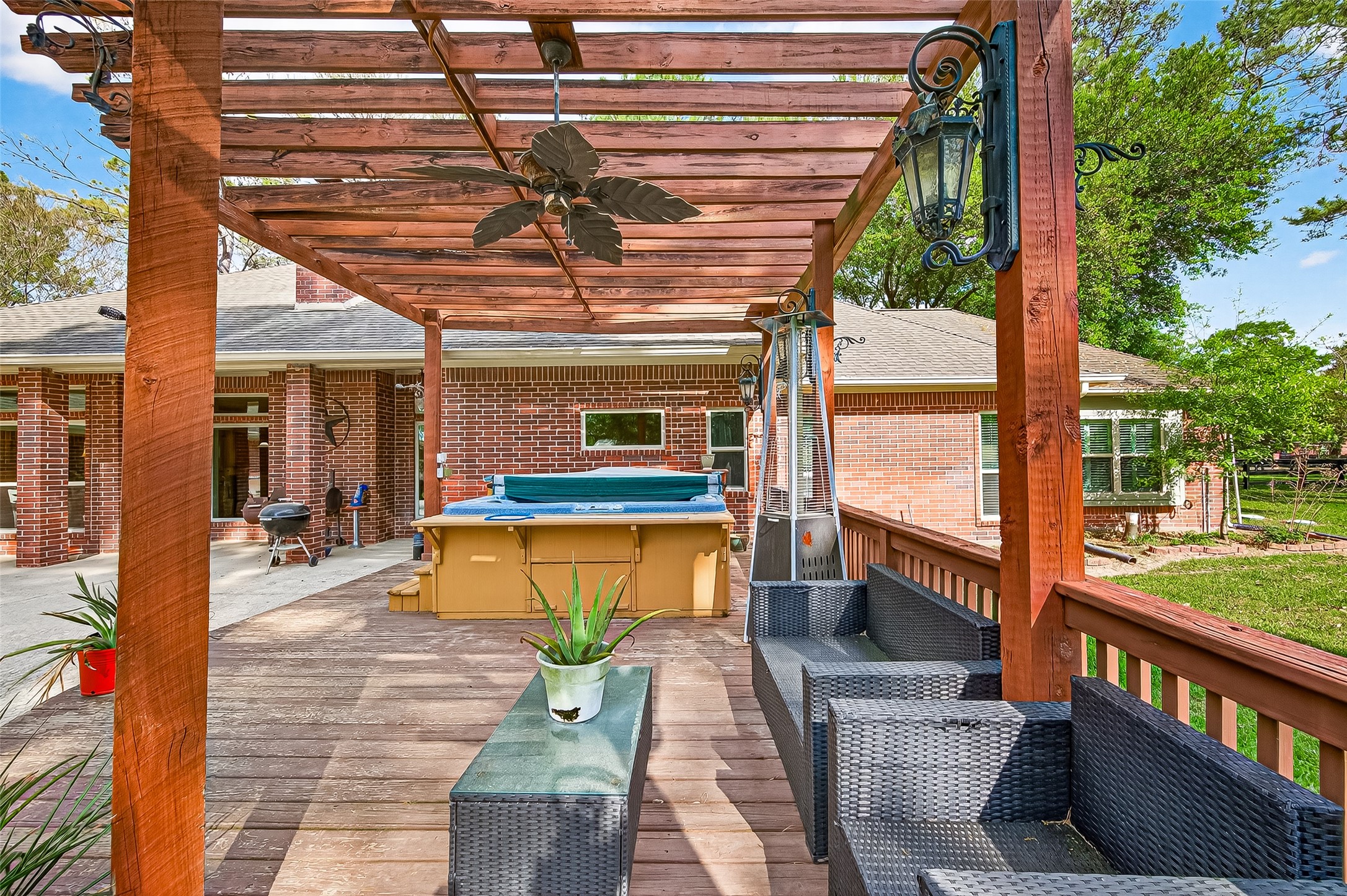 17603 Bending Cypress Road Cypress, TX 77429 - Photo 37 of 43 The outdoor space features a charming wooden pergola with a ceiling fan, stylish seating, and a hot tub. It's perfect for relaxation and entertaining, set against a backdrop of a brick home and lush greenery.
