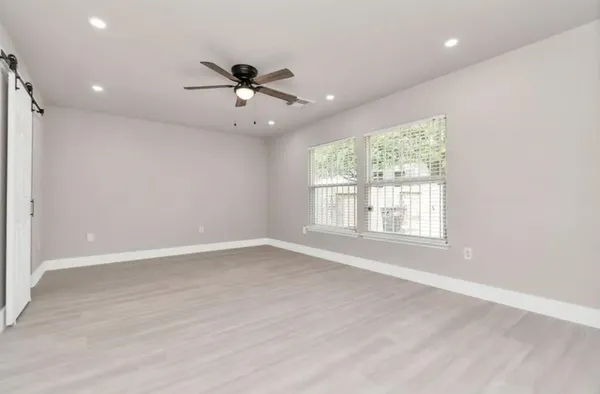 an empty room with wooden floor fan and windows