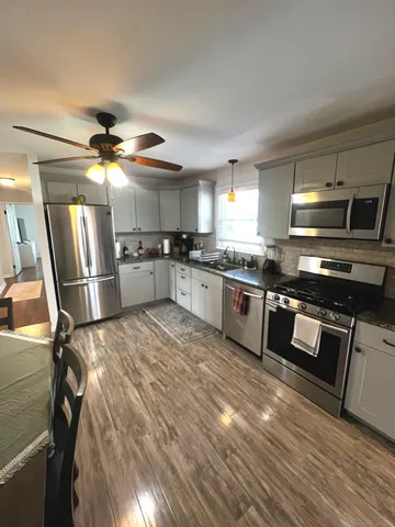 a kitchen with stainless steel appliances granite countertop a stove a sink dishwasher a refrigerator and white cabinets with wooden floor