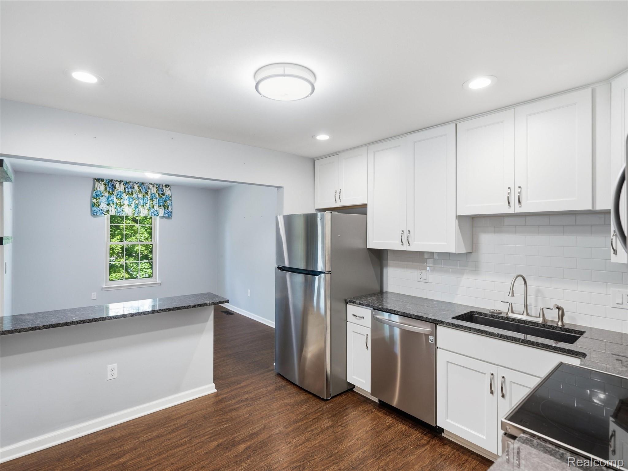 29636 Middlebelt Road, Unit 2602 Farmington, MI 48334 - Photo 15 of 34 Modern kitchen featuring white shaker cabinetry, stainless steel appliances, dark granite countertops, a subway tile backsplash, and wood-finish flooring
