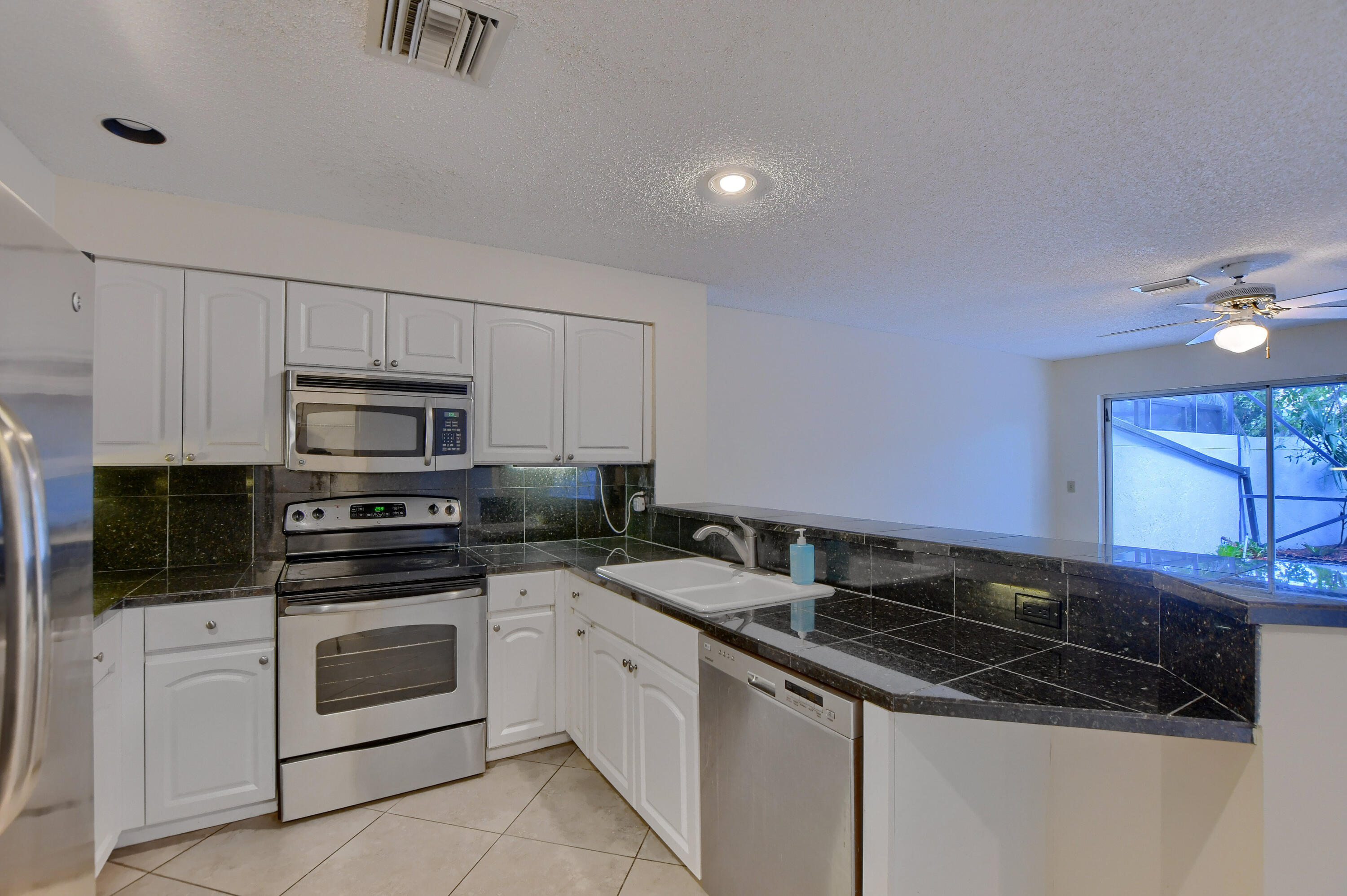 2252 Northwest 53rd Street Boca Raton, FL 33496 - Photo 17 of 41 a kitchen with stainless steel appliances granite countertop a stove a microwave and white cabinets