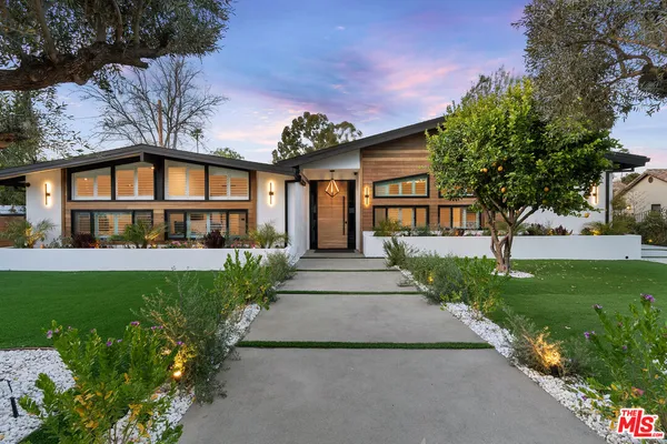 a view of a house with a small yard plants and large trees