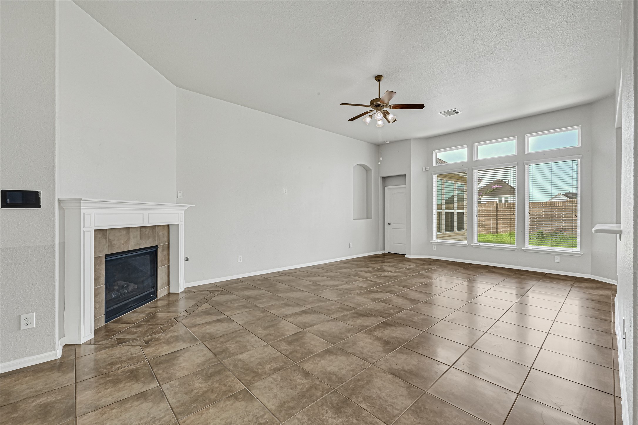 4702 Sedgewood Drive Rosenberg, TX 77471 - Photo 10 of 24 This spacious living room features a cozy fireplace, tiled flooring, and abundant natural light from large windows overlooking the backyard. A ceiling fan adds comfort, and the neutral palette creates a welcoming atmosphere.