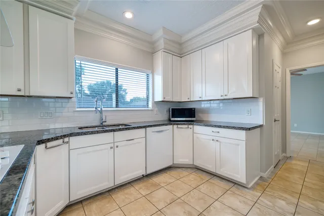 a kitchen with granite countertop white cabinets white appliances a sink and a window