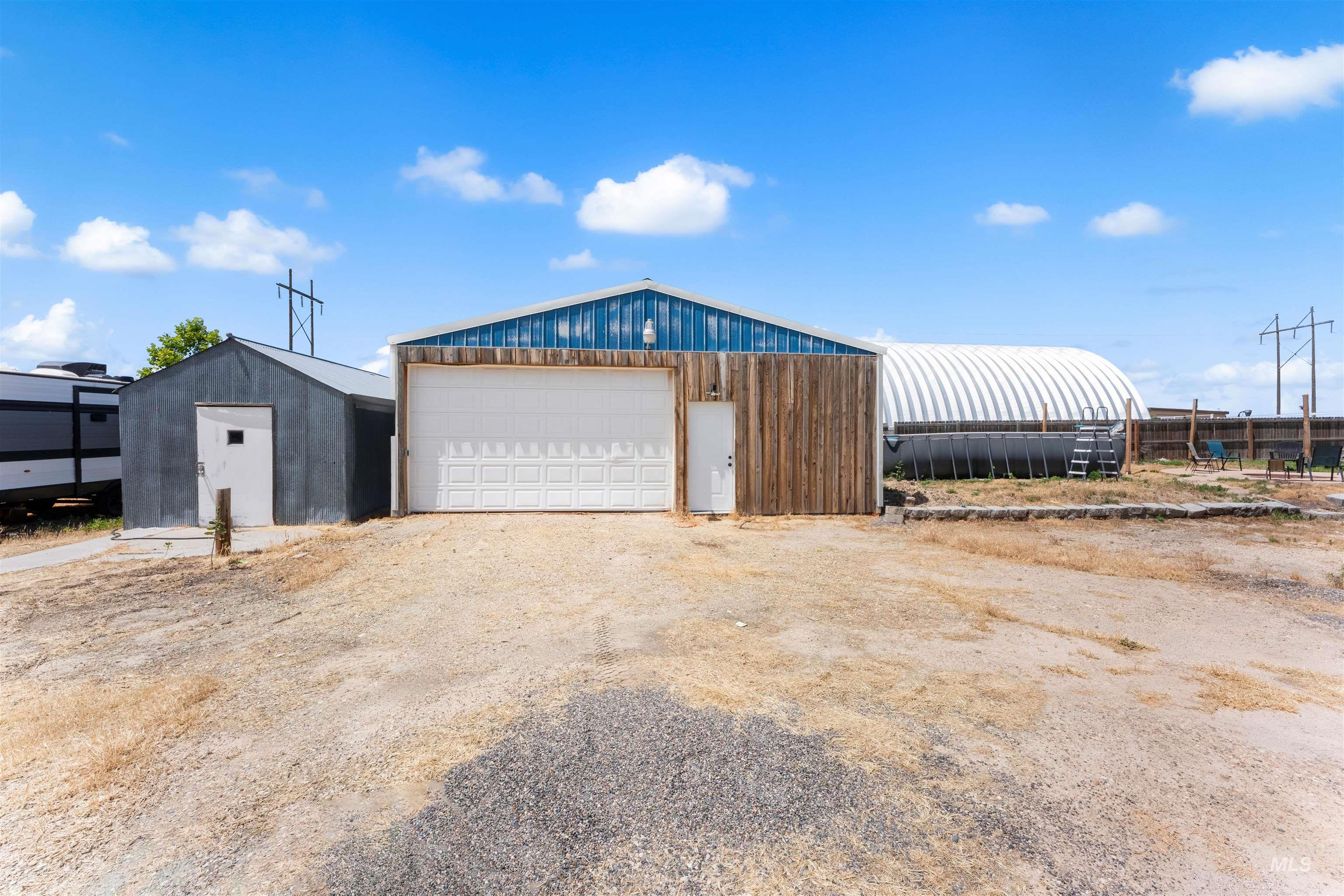 17441 Upper Pleasant Ridge Road Caldwell, ID 83607 - Photo 2 of 40 Large detached structure featuring a white sectional garage door, blue metal siding, and wood-finish paneling