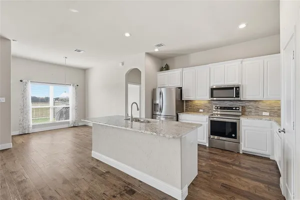 a kitchen with stainless steel appliances a stove top oven a sink a refrigerator white cabinets and wooden floor