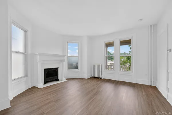 an empty room with wooden floor fireplace and windows
