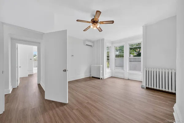 a view of an empty room with wooden floor and a ceiling fan
