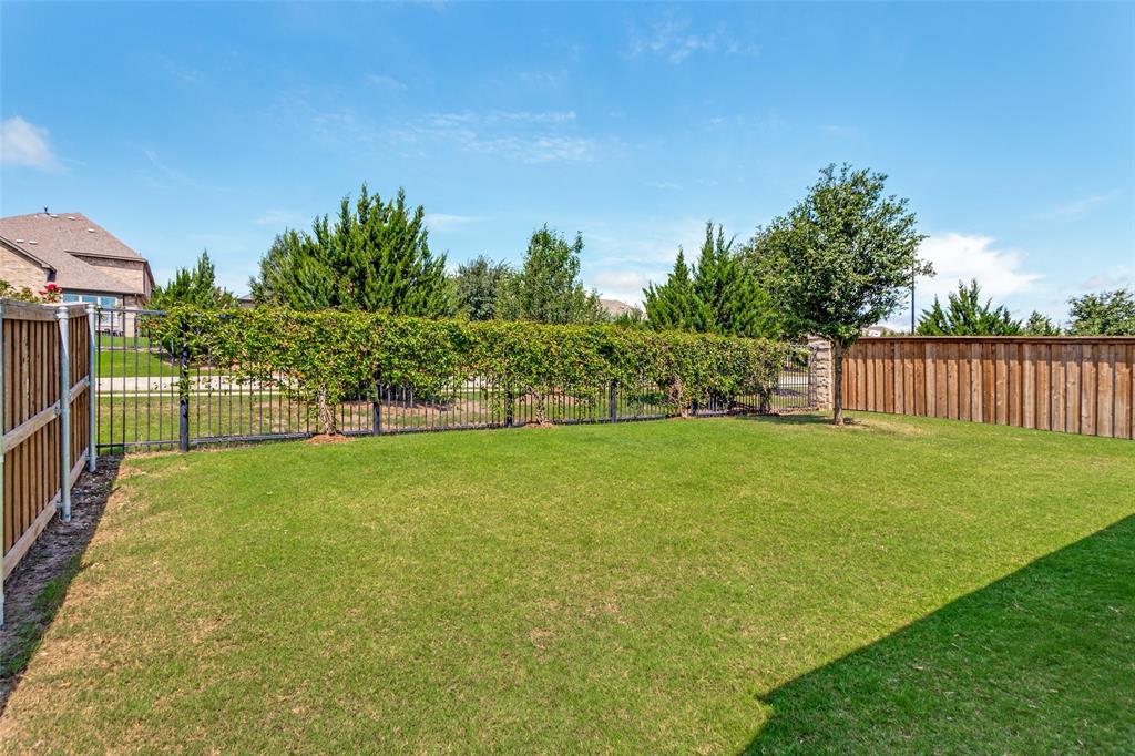 5556 Vaquero Road Fort Worth, TX 76126 - Photo 25 of 25 Expansive grassy backyard featuring a black wrought iron fence, natural wood privacy fencing, mature green trees, and manicured hedges