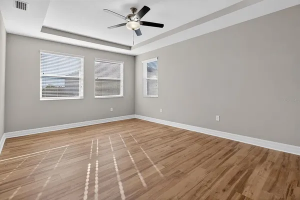 an empty room with wooden floor chandelier fan and windows