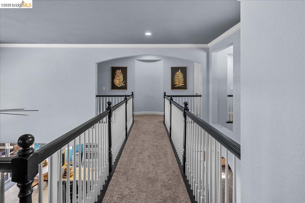 653 Bouma Lane Ripon, CA 95366 - Photo 27 of 39 Carpeted hallway with painted balusters and a dark wood-finish handrail, featuring recessed lighting and archway details