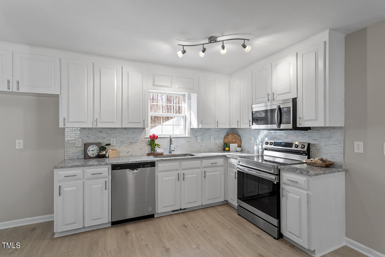 5404 Passenger Place Raleigh, NC 27603 - Photo 7 of 25 a kitchen with stainless steel appliances granite countertop white cabinets a sink dishwasher and a stove with wooden floor