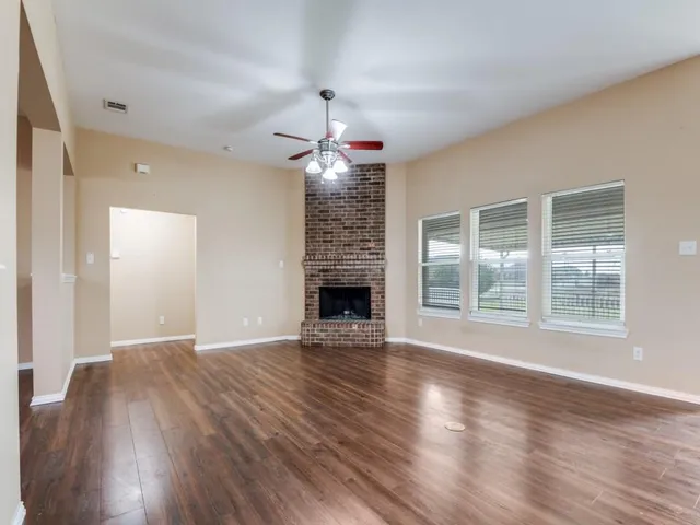 an empty room with wooden floor fireplace and windows
