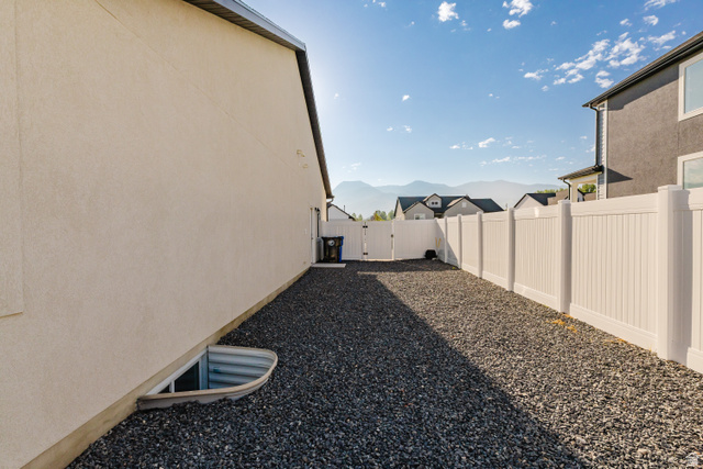 433 North 600 West Smithfield, UT 84335 - Photo 5 of 40 Gravel side yard featuring a white vinyl privacy fence, stucco exterior, and basement window well