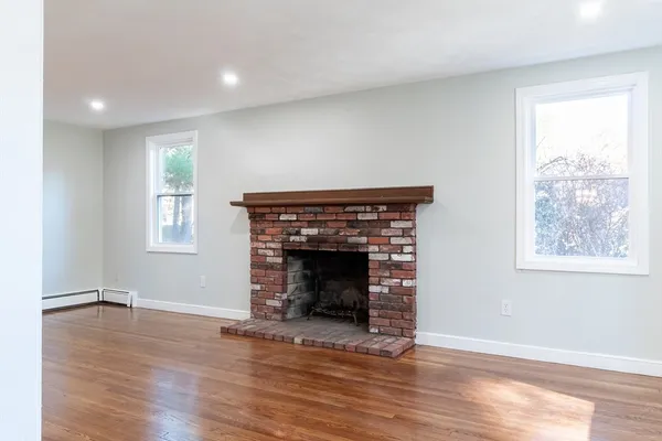 an empty room with wooden floor fireplace and windows