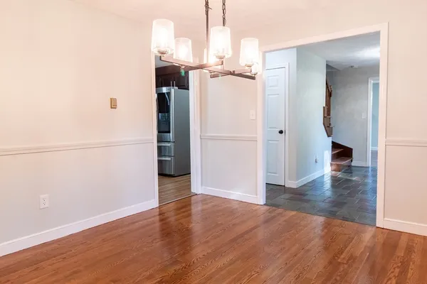 an empty room with wooden floor and way to kitchen