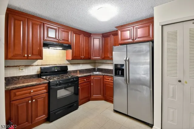 a kitchen with stainless steel appliances granite countertop a stove top oven a refrigerator and dishwasher with wooden cabinets