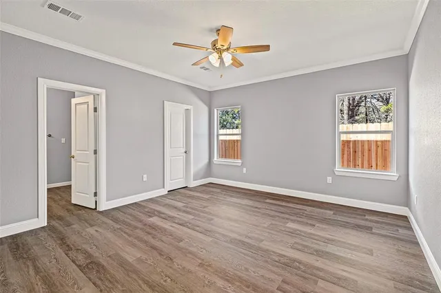 an empty room with wooden floor chandelier fan and windows