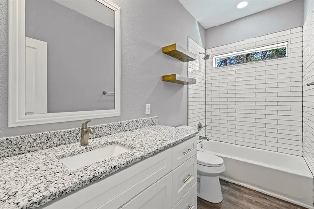 a bathroom with a granite countertop bathtub sink vanity mirror and toilet