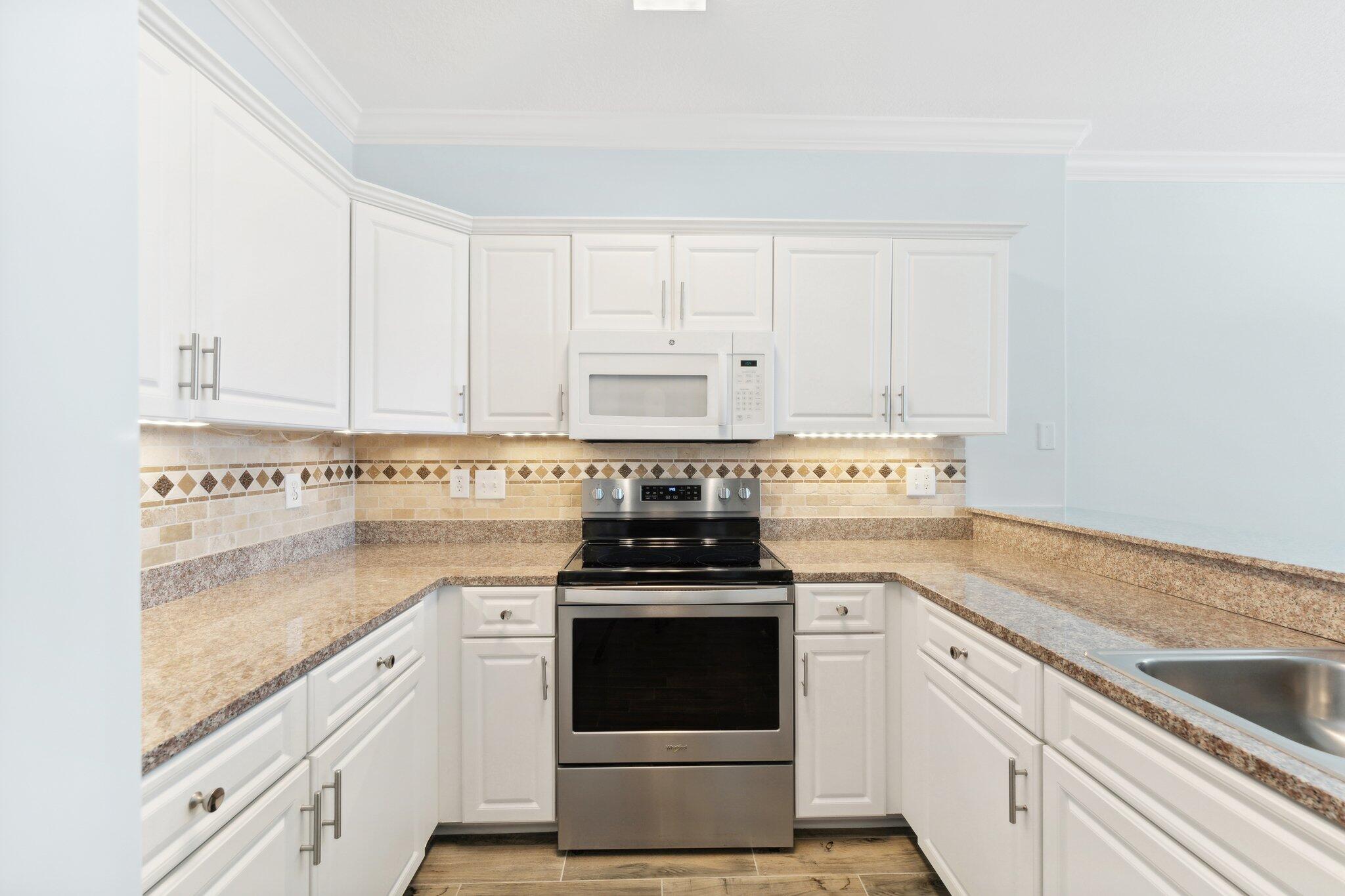 17545 Front Beach Road, Unit 2103 Panama City Beach, FL 32413 - Photo 11 of 56 a kitchen with granite countertop white cabinets and white appliances