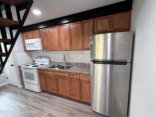 a kitchen with stainless steel appliances granite countertop a refrigerator a sink and a stove with wooden floor