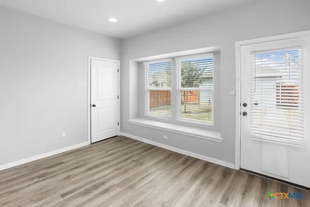 a view of an empty room with wooden floor and a window