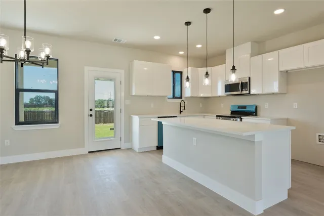 a kitchen with kitchen island a white counter top space stainless steel appliances and a chandelier