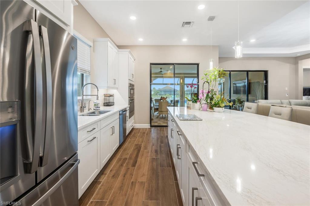 8416 Rosa Court Naples, FL 34114 - Photo 9 of 34 Modern kitchen featuring an expansive island with a light-toned countertop, white cabinetry with contemporary hardware, stainless steel appliances, and wood-finish flooring