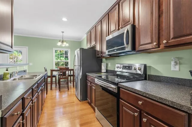 a kitchen with stainless steel appliances granite countertop a stove top oven a sink a dining table and chairs with wooden floor