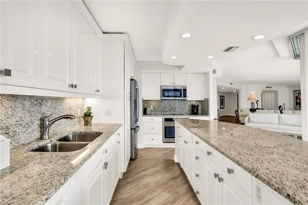 a large white kitchen with stainless steel appliances granite countertop a lot of counter space and wooden floors